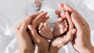 Nyfødt baby sine føtter omkranses av voksne hender