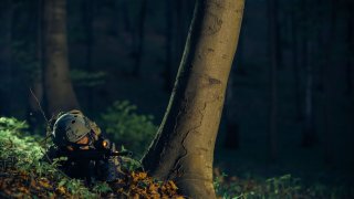 Soldat som ligger med våpen i skogen