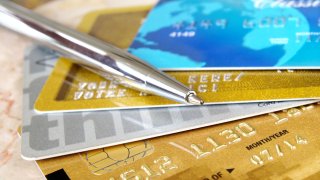 Nærbilde av fire kredittkort som ligger spredd utover som en vifte, med en sølvfarget kulepenn oppå.