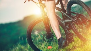 Mann på sykkel i grønne omgivelser, nærbilde av den sorte sykkelen og mannens bein
